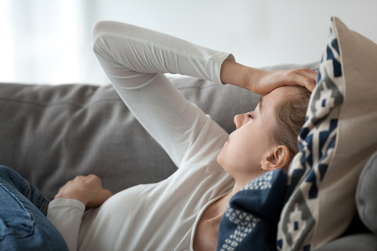 Woman lying on a couch with her hand on her head.